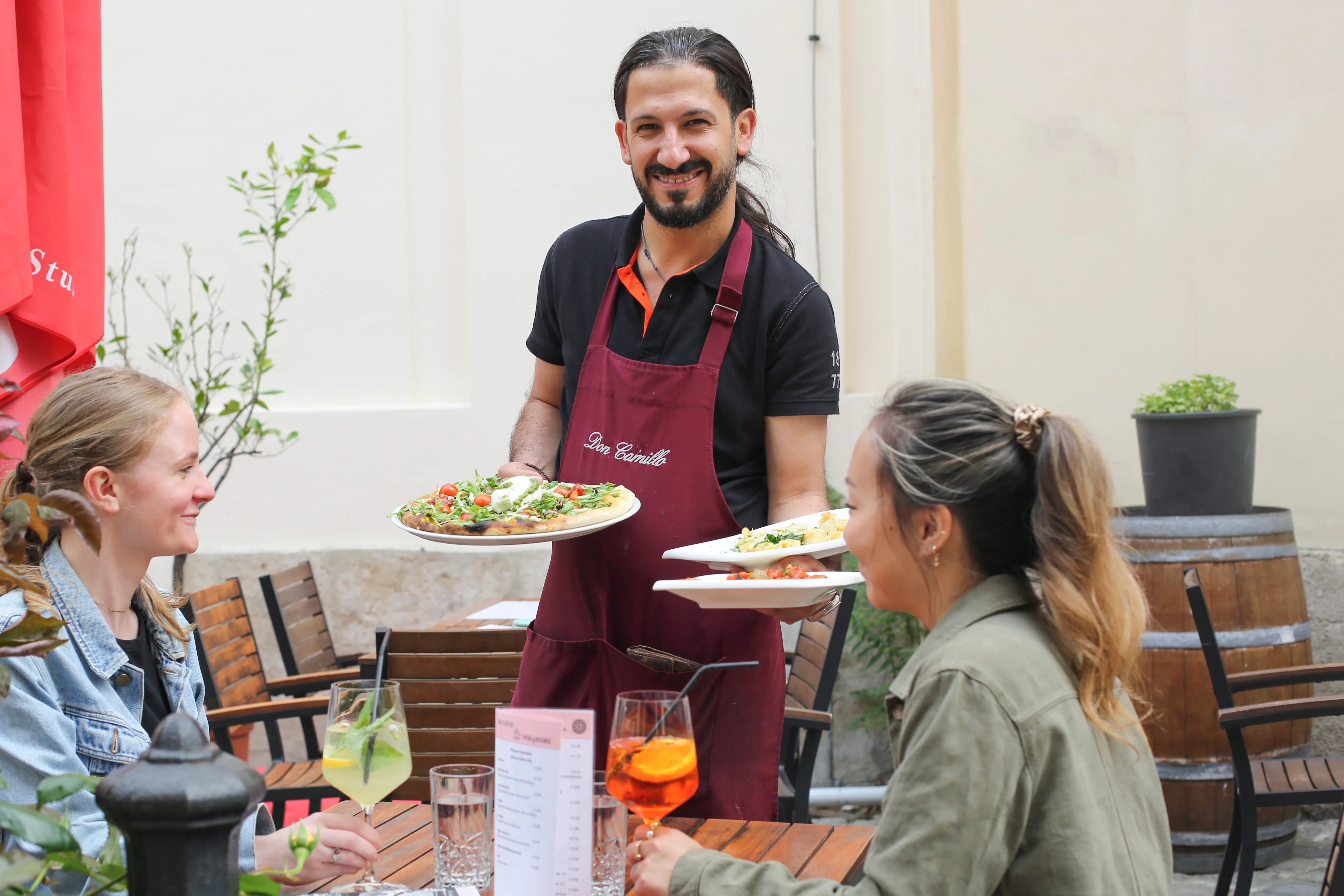 Kellner serviert Pizza und Pasta im Gastgarten